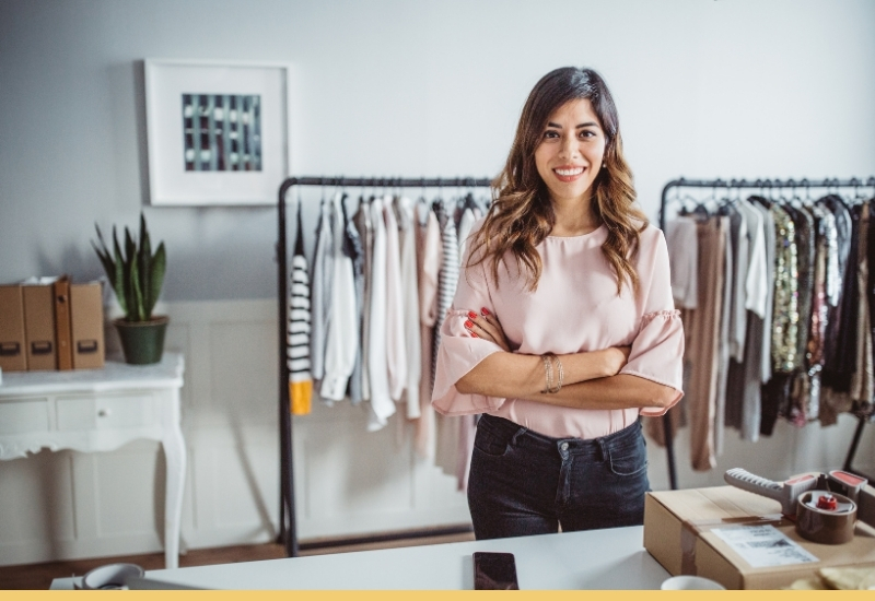 Small business owner standing at a desk with product on clothing racks behind them